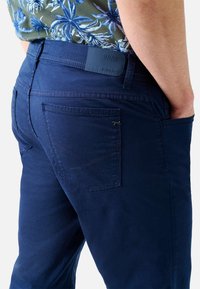 Brax ultralätta marinblå byxor med en slät yta, utrustade med bakfickor med korsstygn och en märkesmidjad.