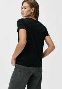 Czarny t-shirt z krótkim rękawem i okrągłym dekoltem, wykonany z bawełny, o gładkiej fakturze i luźnym kroju, w zestawieniu z szarymi dżinsami.