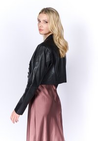 Giacca cropped in pelle nera con una texture liscia e collo elegante, abbinata a un vestito rosa in satin con un drappeggio morbido.