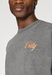 Γκρι φούτερ με λαιμόκοψη, που διαθέτει πορτοκαλί κέντημα με την ένδειξη "City" στ�ην αριστερή πλευρά του στήθους. Μαλακό, ελαφρώς υφασμένο ύφασμα.