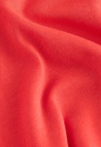 Tissu corail avec une surface lisse et légèrement texturée, présentant des plis doux et un drapé élégant. Le matériau est léger et respirant.