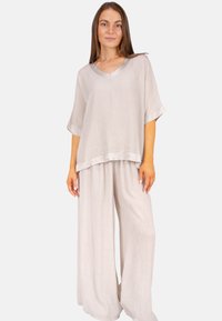 Leichtes, locker sitzendes Zweiteiler-Outfit in sanftem Beige, bestehend aus einem V-Ausschnitt-Oberteil mit kurzen Ärmeln und weit geschnittenen Hosen aus strukturiertem Stoff.