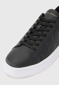 Svart lær sneakers med flate lisser, teksturert sidemønster og hvit gummisåle. Logo preget på tungen.