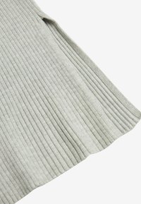 Tissu tricoté côtelé gris clair avec un motif vertical, plié sur le bord, montrant une texture douce et une épaisseur.