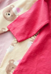 Wyświetlono dwa bawełniane t-shirty: jeden różowy o gładkiej fakturze, a drugi kremowy z nadrukowanymi uroczymi niedźwiadkami i zwierzętami.