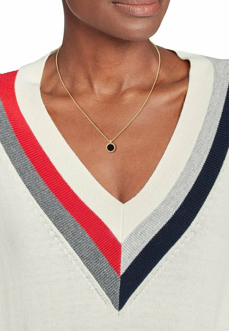 Crèmekleurige V-halstrui met rode, grijze en marineblauwe strepen langs de halslijn. Bevat een delicate gouden ketting met een zwarte ronde hanger.