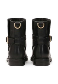 Black leather ankle boots with a smooth finish, featuring a gold metal hardware accent, adjustable strap, and flat rubber sole.