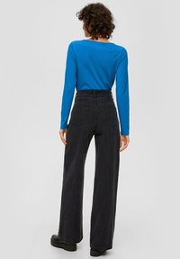 Schwarze weit geschnittene Jeans mit hoher Taille und hinteren Taschen. Kombiniert mit einem blauen Langarmhemd und knöchellangen schwarzen Stiefeln.