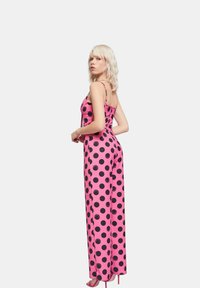 Mono rosa sin mangas con grandes lunares negros. Presenta tirantes finos, un cuerpo ajustado y una parte inferior de pierna ancha. Textura de tela suave.