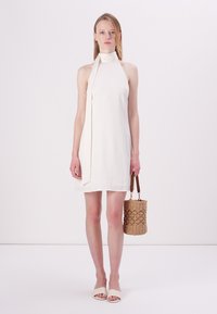 Balta, bez piedurknēm, kleita ar augstu apkakli un izšūtu sānu detaļu. Saskaņota ar austu, cilindrisku somu un plakanām, gaišām sandalēm.