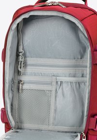 Červený batoh uvnitř s světle šedým podšívkou, obsahující zipové kapsy, elastické kapsy a síťovou přihrádku pro organizaci.