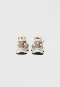 Dva sportska tenisica svijetlosmeđe gornje površine, tamnosmeđi detalji i sivi detalji. Teksturirani materijal s mekanom potplatom i dizajnom loga.