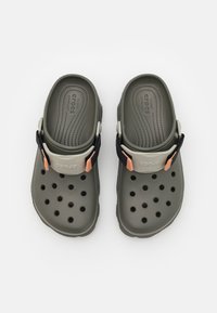 Sandales à enfiler moulées vert foncé avec des trous de ventilation, une sangle noire contrastante et des accents orange. Semelle intérieure texturée pour une meilleure adhérence.