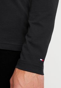 Langärmliges schwarzes Shirt aus Baumwolle mit einem kleinen dreifarbigen Logotag am Bündchen und einer glatten Textur sowie sauberem Nähen.