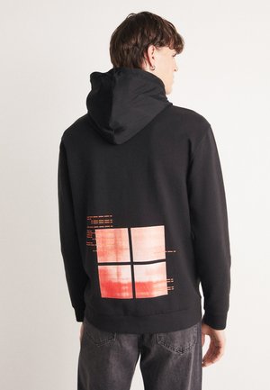 Hoodie noir avec une capuche texturée et un imprimé graphique à l'arrière représentant quatre carrés rouges et oranges, sur fond noir.
