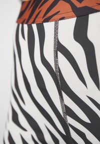 Leggings a vita alta con stampa zebra bianco e nero, caratterizzati da una fascia in brown a contrasto e cuciture nere visibili lungo le cuciture.