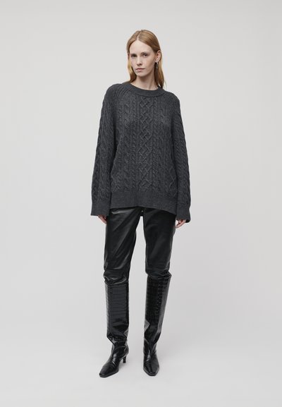 Dunkelgrauer gestrickter Pullover mit Kabelstruktur, lässiger Schnitt, kombiniert mit schwarzen Kunstlederhosen und kniehohen gemusterten Stiefeln.