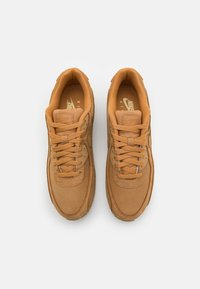 Beiga Nike Air-sneakers är tillverkade av en kombination av mocka och mesh-material, har en rund tå, platta snören och en texturerad gummisula.