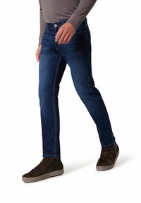 Dunkelblaue Jeans aus Denim mit geradem Bein, dezent sichtbaren Nähten und Knopfverschluss, kombiniert mit braunen High-Top-Sneakern.