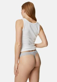 Witte tanktop met een aansluitend ontwerp. Lichtblauwe kanten slip met een ingewikkeld patroon en golvende randdetails.