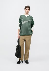 Zöld-fehér csíkos pulóver bordázott mandzsettákkal, bézs kordbársony nadrág és fekete válltáska. Fekete sportcipők fehér részletekkel.