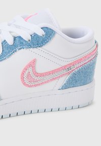 Baskets blanches avec des accents en denim, des lacets blancs et un swoosh Nike pailleté rose entouré de sequins argentés.