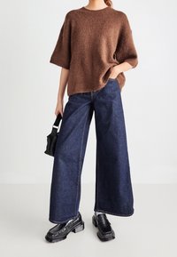 Pull en maille marron doux avec un col rond, accompagné d'un jean denim foncé à jambes larges. Des mocassins noirs complètent la tenue.
