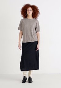Grijze oversized t-shirt, zwarte enkellange rok, crèmekleurige broek en zwarte enkellaarsjes. Eenvoudig ontwerp met een ontspannen pasvorm in zachte stoffen.