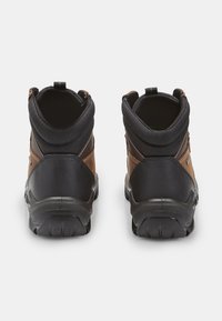 Barna és fekete vízálló túracipők masszív gumitalppal, párnázott bokarésszel és megerősített varrásokkal, amelyek szabadtéri tevékenységekhez készültek.