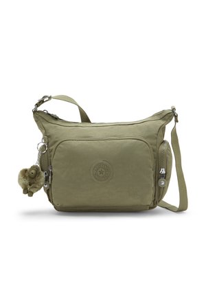 Olivgroene crossbodytas met ritssluitingen aan de voorkant en zijkant en een klein pluchen sleutelhanger bevestigd aan de ritssluiting.