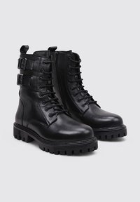 Bottes de combat en cuir noir avec un bout rond, des lacets à l'avant, une fermeture éclair sur le côté et deux accents de boucle sur la tige. Semelle épaisse et texturée.