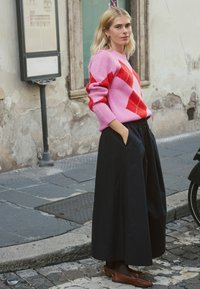 Roze trui met rood diamantenpatroon, zwarte maxirok en bruine loafers. Trui heeft geribbelde manchetten; rok heeft zijzakken.