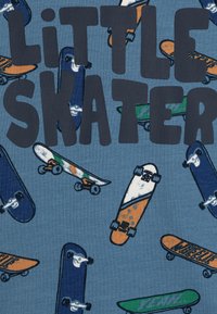 Sininen kangas, jossa on hajallaan oransseja, vihreitä ja valkoisia skeittikuvastoja. Teksti "KAMPPAILIJAPIKKU" on selvästi esillä tummansinisellä.