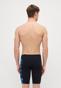 Shorts de bain noirs au design ajusté, avec un motif géométrique bleu sur le côté. Fabriqués en matériau léger et extensible.
