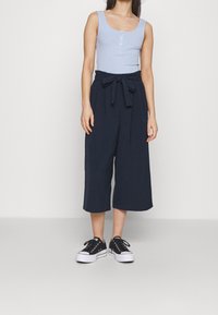 Light blue ribbed tank top with buttons, paired with navy culottes featuring a tie waist. Black and white sneakers complete the look.