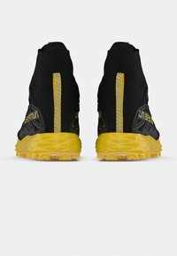 Melnas taku skriešanas kurpes ar dzeltenu zoli, teksturētu virsmu, augstu potītes atbalstu un atstarojošiem elementiem aizmugurē.