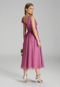 Une robe sans manches, longueur genou, en tissu violet doux avec un corsage ajusté, des détails de manches volantes et une jupe fluide. Assortie à des talons argentés.