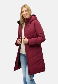 Bordeaux lang puffer-frakke med hætte, der har et quiltet design, lynlåslukning og en tekstureret finish. Brun accentdetalje synlig.