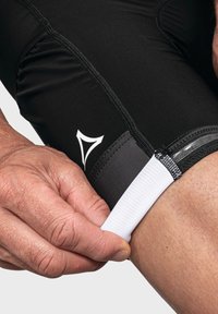 Schwarze Radhosen mit glatter Textur, ausgestattet mit einem weißen elastischen Bund und dezenter Markenkennzeichnung, die am Saum angepasst werden.