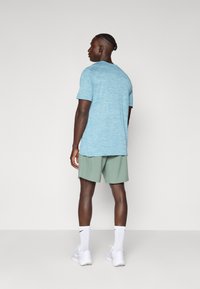 Himmelblaues, strukturiertes Kurzarmhemd, kombiniert mit mintgrünen Shorts. Abgerundet wird der Look mit weißen Sportsocken und Schuhen.