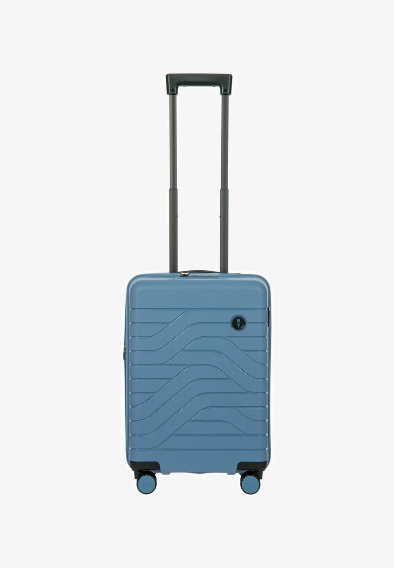 Valigia rigida di colore azzurro chiaro con design ondulato in rilievo, manico e ruote nere. Presenta una chiusura a zip e un dettaglio con logo sulla parte anteriore.