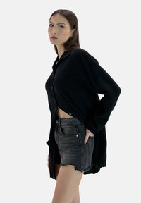 Sort, tekstureret langærmet skjorte med knaplukning, båret åben over højtaljede, slidte grå denimshorts.