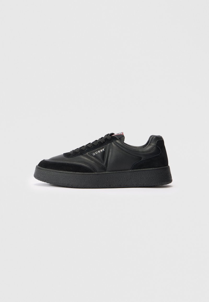 Black low-top sneaker with thick sole, lace-up front, suede and leather panels, and "GUESS" logo on the side.