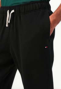 Schwarze Sweatpants aus weichem Stoff, ausgestattet mit einem elastischen Bund mit Kordelzug und einem kleinen Logo in Rot, Weiß und Blau.