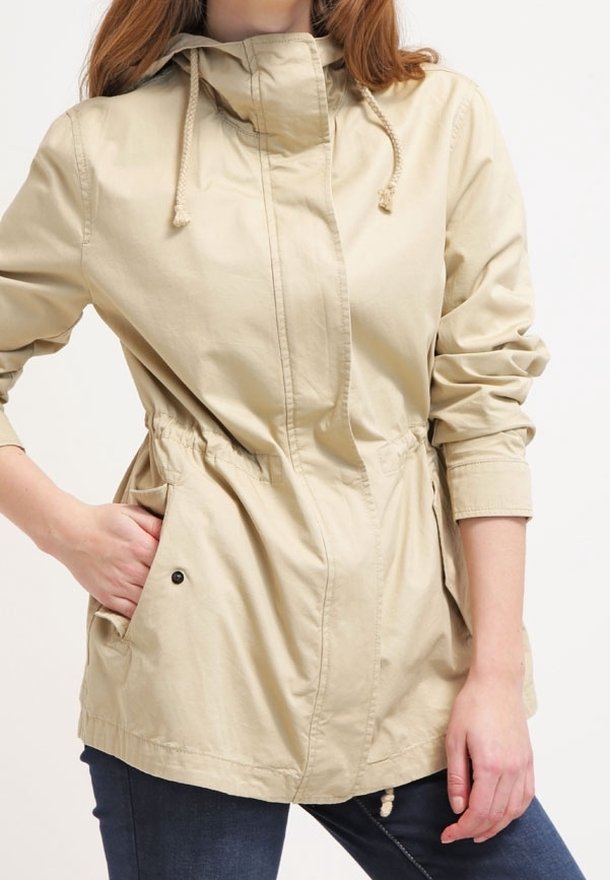 Ljust beige jacka med framdragkedja, dragsko huva, elastisk midja och två sidofickor. Tillverkad av bomull med en mjuk yta.