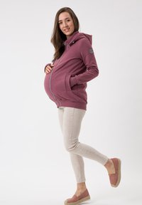 Felpa premaman color malva, con zip anteriore, tasche laterali e cappuccio regolabile. Abbinata a jeans skinny beige chiaro e espadrillas rosa con zeppa.