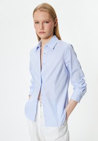 Hellblau- und weißgestreiftes Button-up-Hemd mit Kragen, langen Ärmeln und Seitentaschen. Es hat eine lockere Passform und eine glatte Stofftextur.