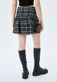 Jupe mini à carreaux noir et blanc avec des volants superposés ; accompagnée de bottes en cuir noir montantes avec des semelles épaisses.