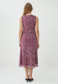 Mouwloze bordeauxrode jurk met wit stippenpatroon, vloeiende stof, knielange zoom en getailleerde taille. Minimalistisch ontwerp, geen zichtbare hardware.