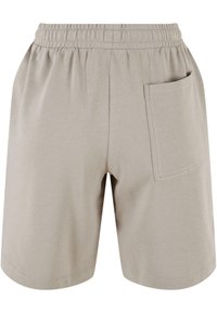 Shorts beige à taille élastique avec une seule poche rectangulaire sur le côté droit et des détails de couture visibles.